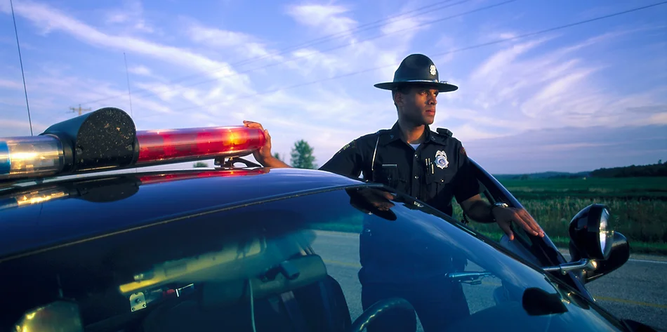 Stock photo of police officer standing next to police car and looking into the distance
