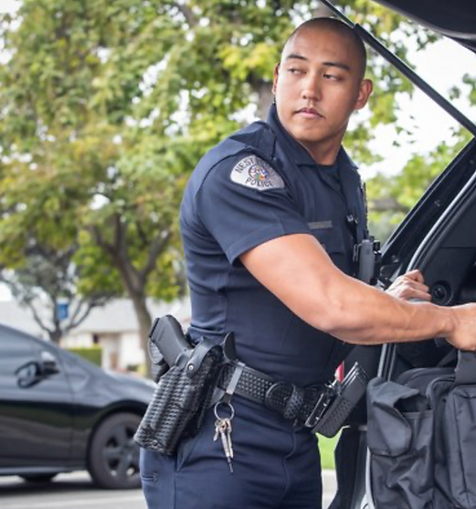 Asian-American police officer in uniform looking behind him while picking up duffel bag from back of open SUV