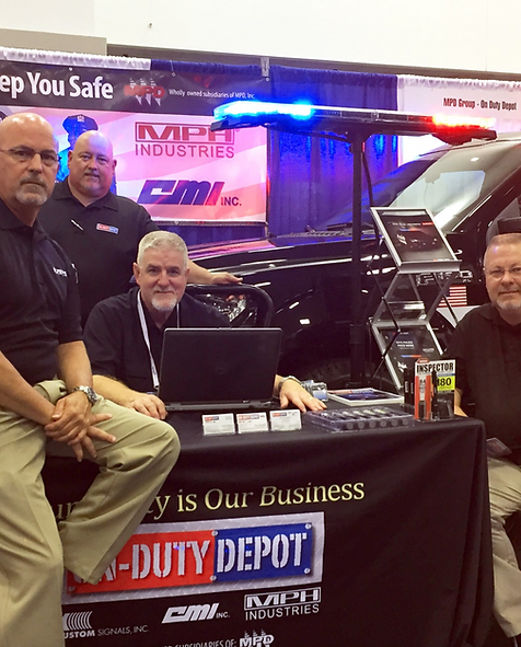 Several guys from On Duty Depot at trade show booth with vehicle, light bar, and banners in background